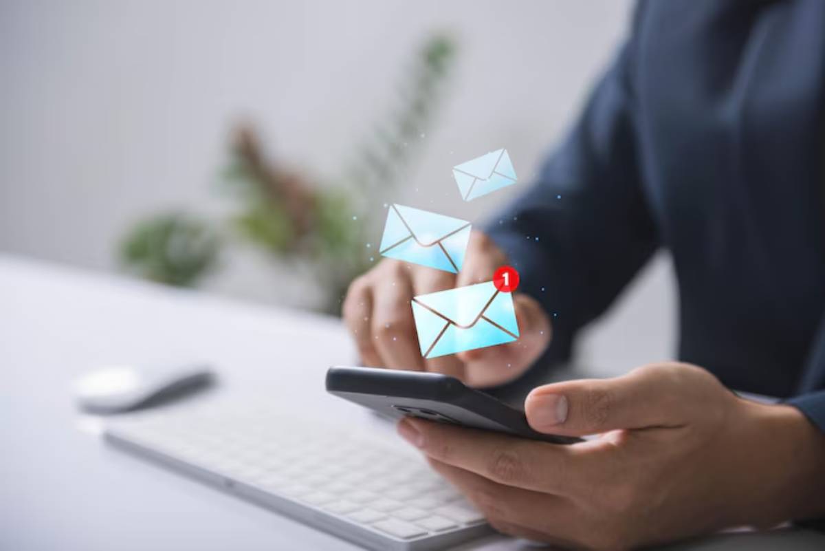 A person using a smartphone with floating email icons and a notification for a new message above their hand, with a keyboard in the background.
