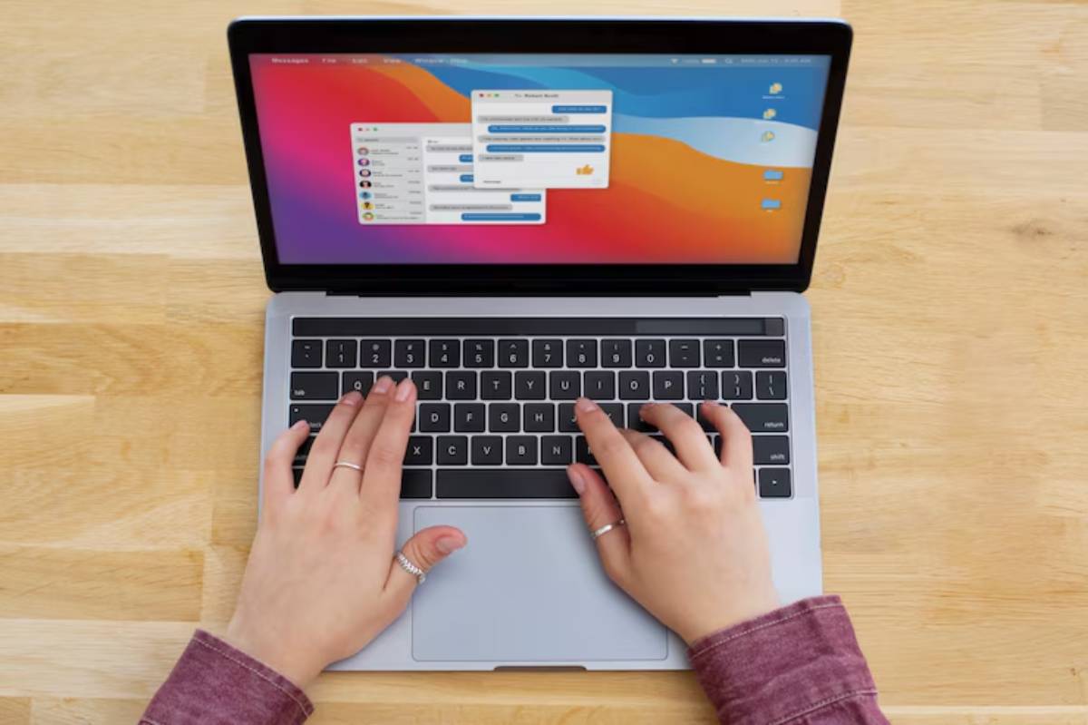 Person typing on a laptop displaying a messaging app against a wooden table background.