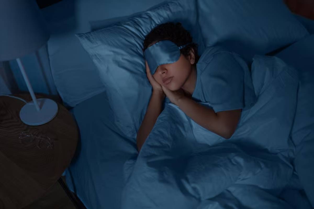 A person lies in bed, covered in light blue sheets, with hands clasped together in a peaceful, serene ambiance created by dim lighting.