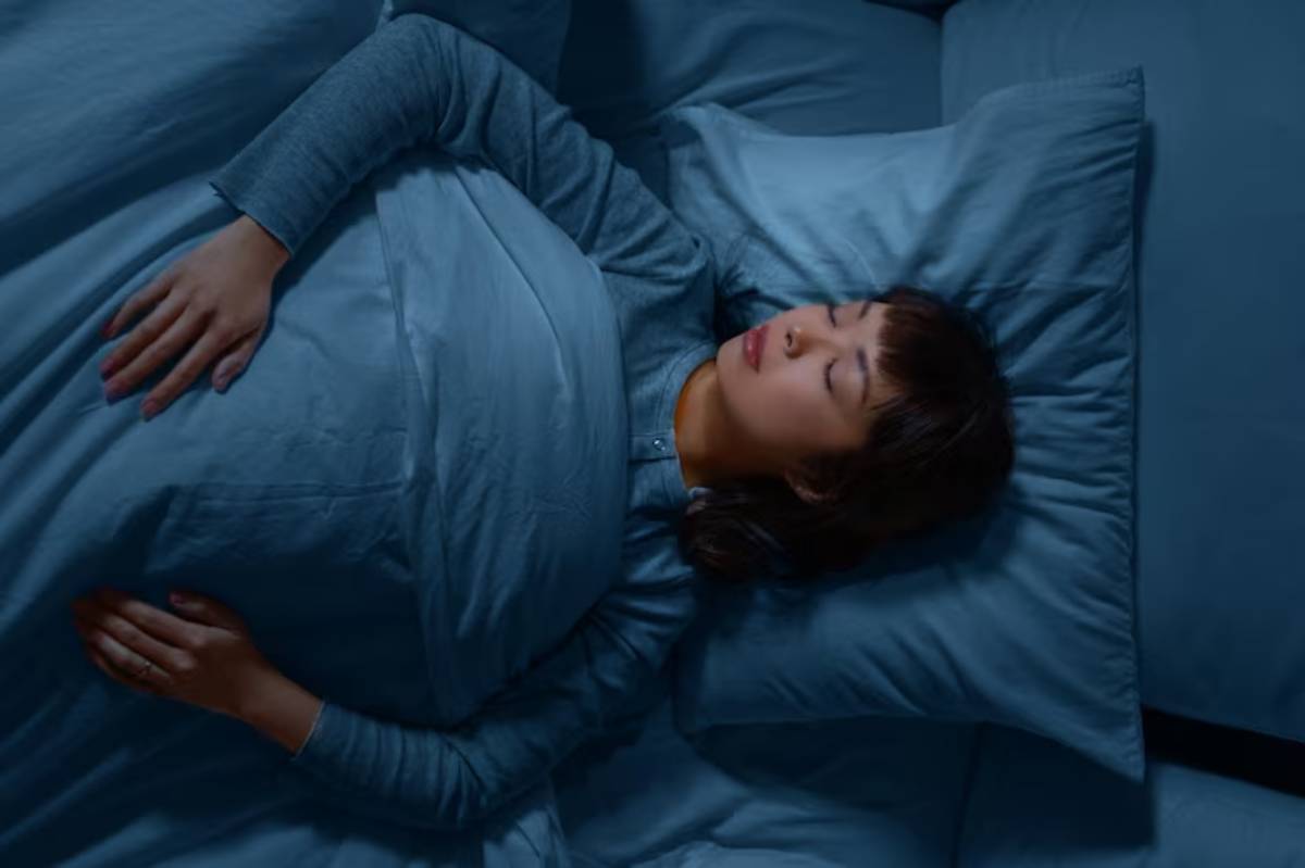 A person lies peacefully in bed, covered with a cozy blue blanket and surrounded by matching blue pillows, in a serene sleeping posture.