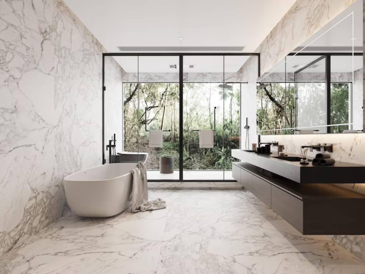 Modern bathroom with marble walls, a freestanding tub, sleek black fixtures, and large glass doors opening to a green outdoor view.