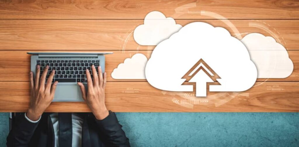 A person's hands typing on a laptop with a cloud upload symbol above, symbolizing cloud computing and data storage.