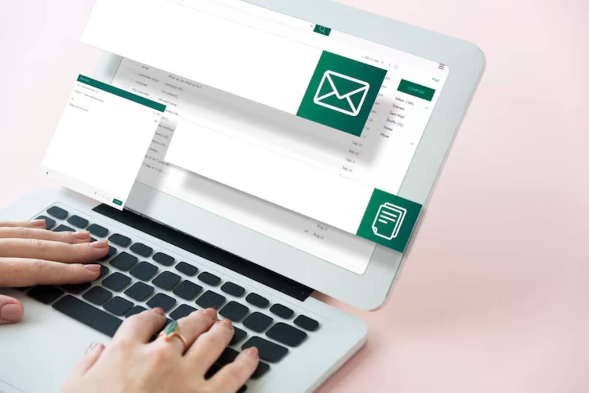 A person types on a laptop displaying email and document management interfaces, against a soft pink background.