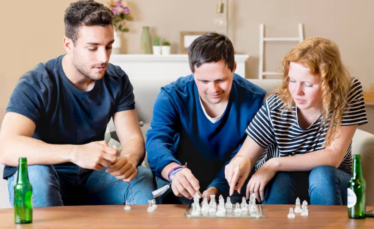 Three friends engaged in a chess game on a wooden table, with drinks beside them, in a cozy living room setting.