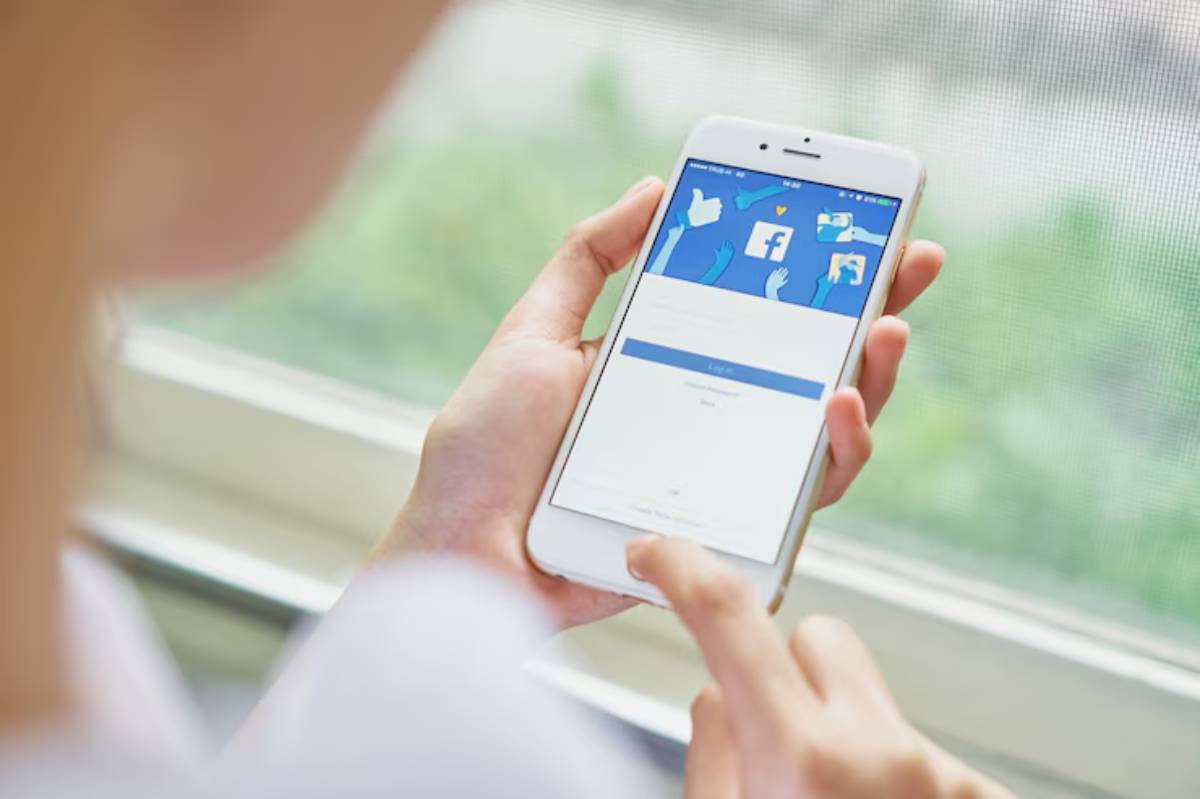 A person logging into Facebook on a smartphone with a focus on the login screen, viewed from a window in natural light.
