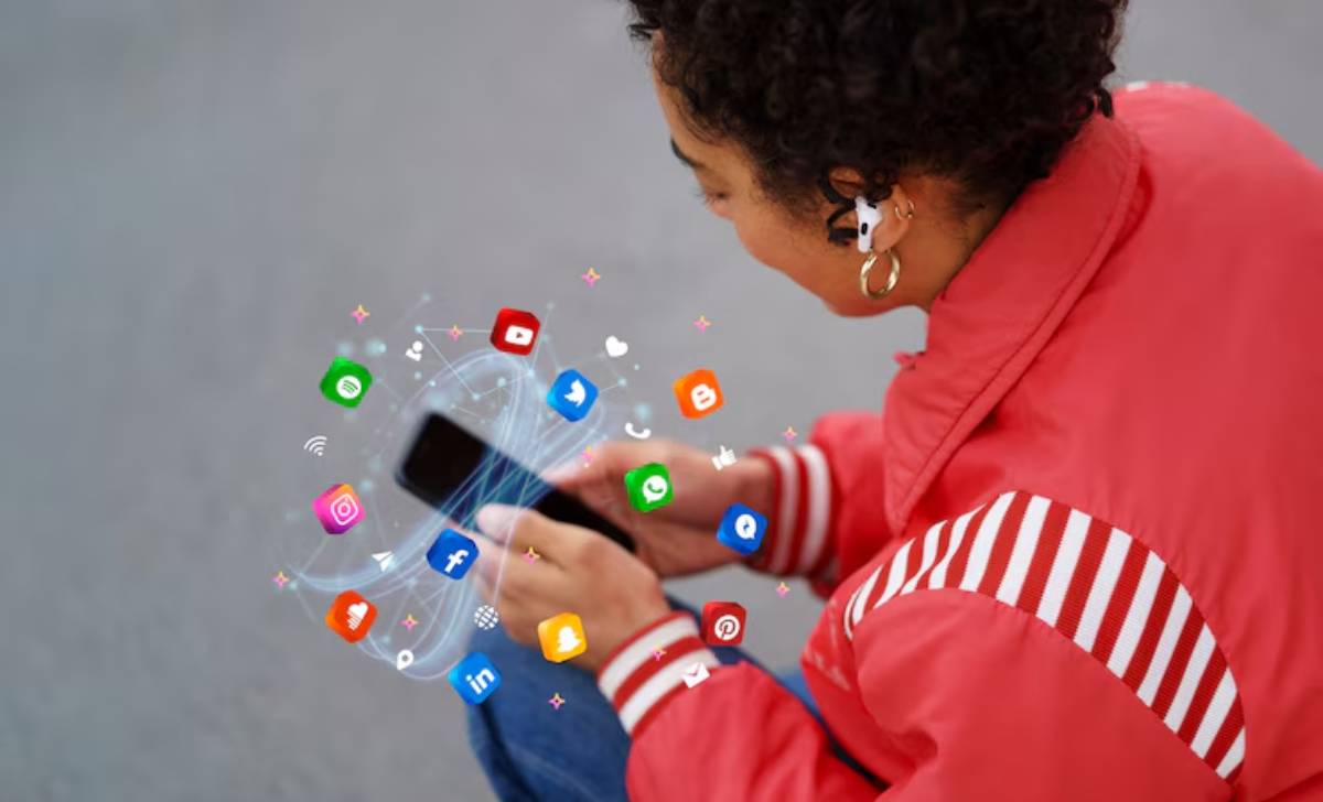 A person in a red jacket holds a smartphone, surrounded by colorful social media app icons floating around them.