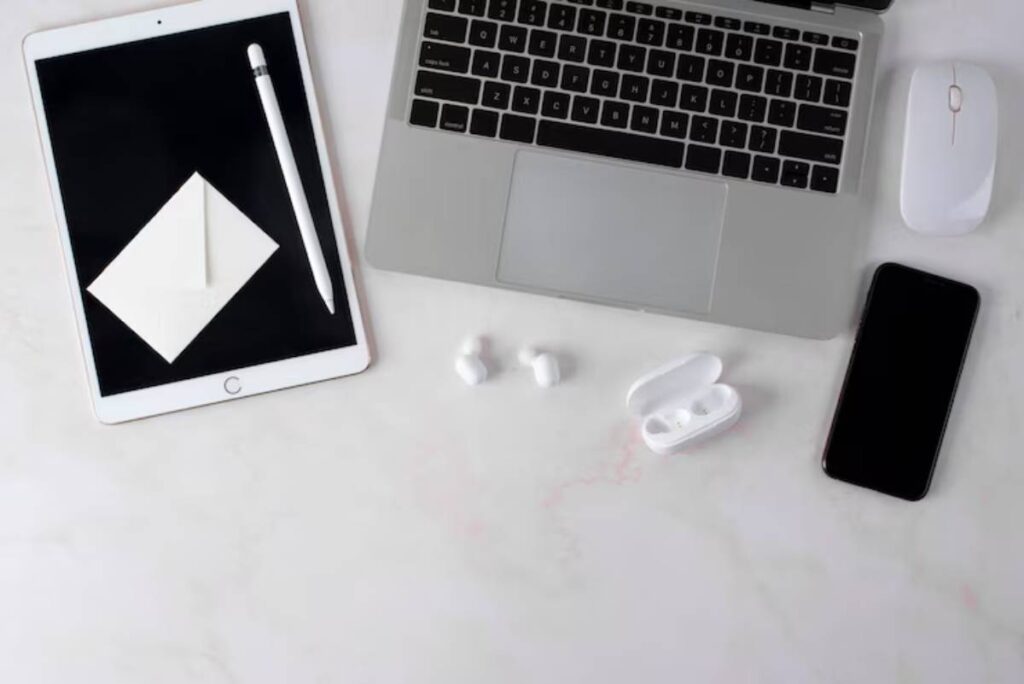 A sleek workspace featuring an iPad, MacBook, smartphone, wireless earbuds, a mouse, and a stylus on a marble surface.