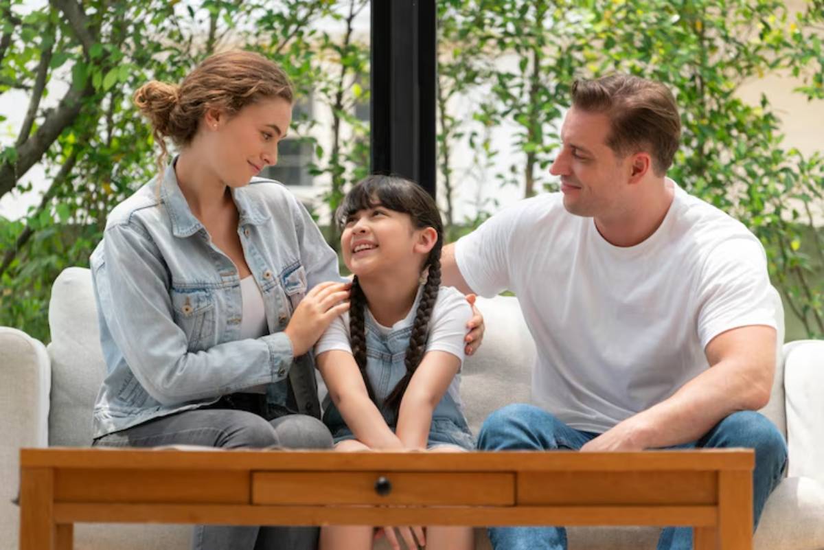 A family sits together on a couch, surrounded by greenery, sharing a moment of connection and warmth.