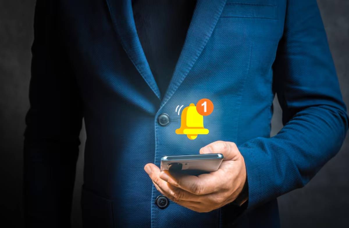 A man in a blue suit checks his phone, displaying a notification with a ringing bell icon, indicating an alert or message.