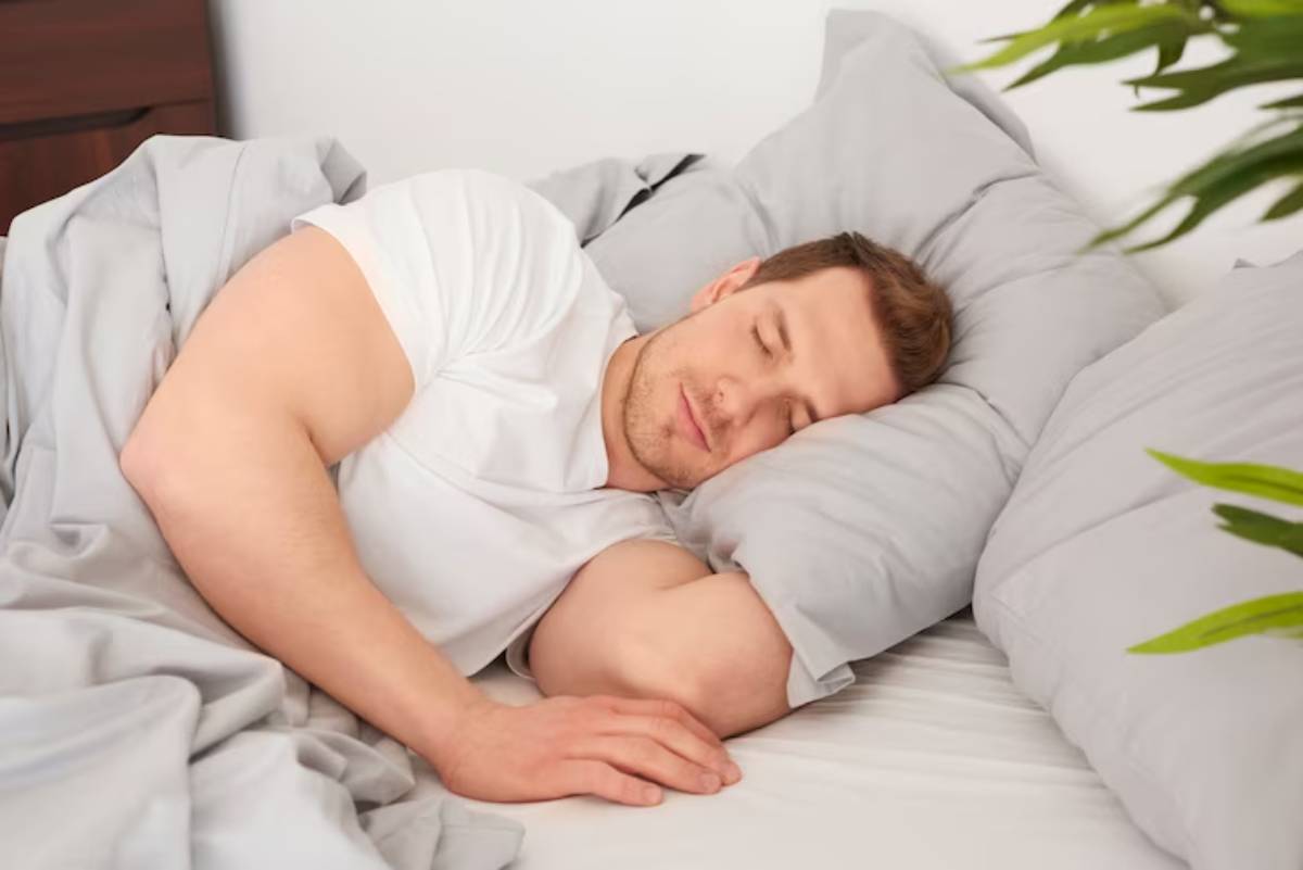 A person lies peacefully in bed, surrounded by soft gray blankets and pillows, creating a serene and cozy atmosphere.
