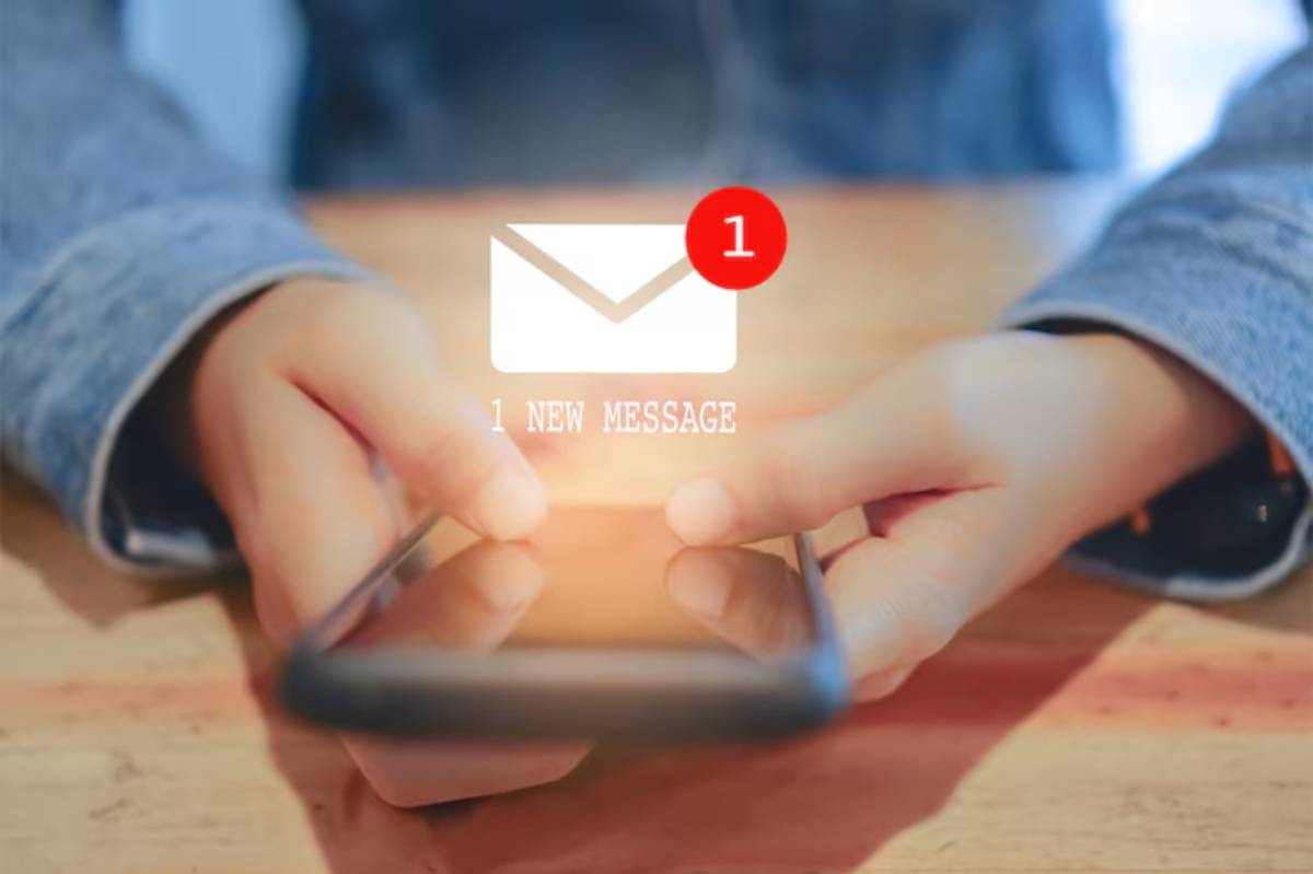 A person holding a smartphone with a notification for one new message displayed on the screen, set against a wooden table.