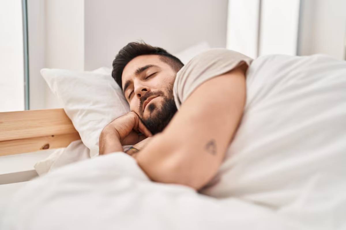 A person is comfortably lying in bed, surrounded by white pillows and blankets, with a cozy, serene atmosphere.